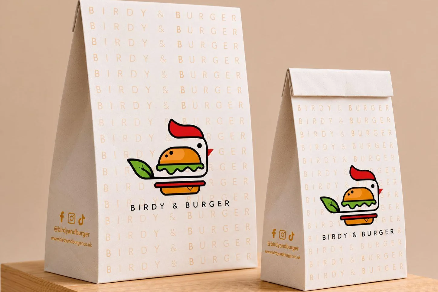 Two Birdy & Burger takeaway bags, white with the orange name repeated and the logo on the front